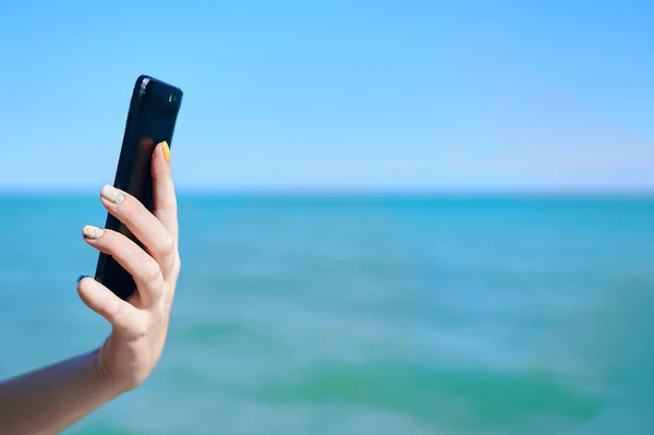 Smartphone in womans hand on sea background.