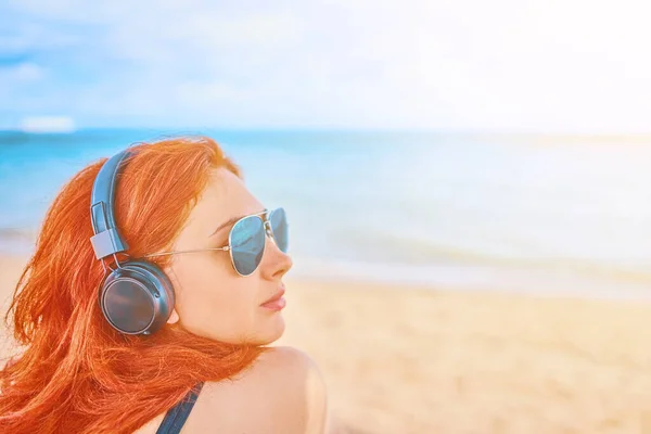 Beautiful woman in sunglasses listening to music on the beach.