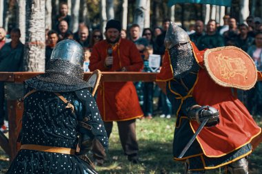 Zırhlı ve miğferli şövalyeler, arenada kılıç ve kalkanlarla savaşıyorlar..