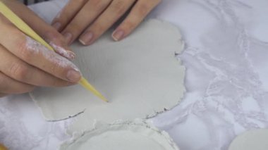 Kadın, ahşap alet ve kırtasiye bıçağı kullanarak kil tabakasından şekil veriyor..