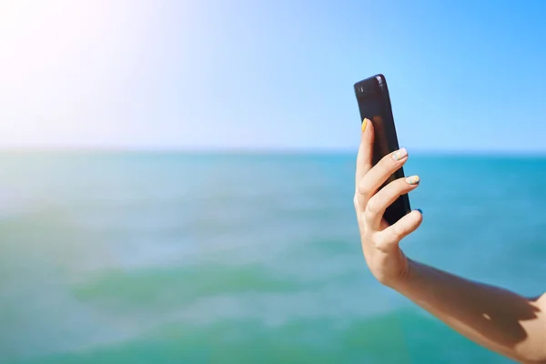 Smartphone in womans hand on sea background.