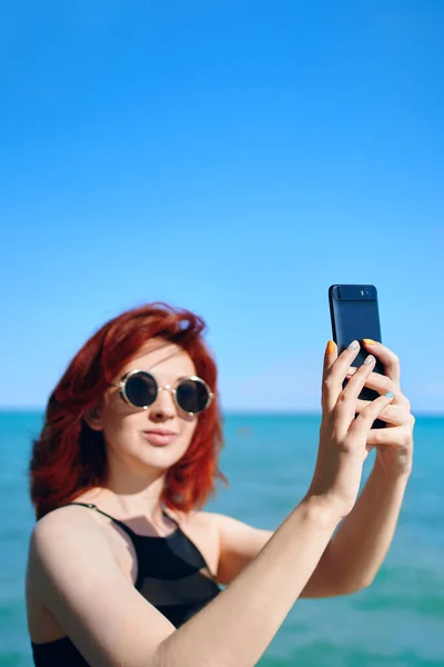 Рыжая женщина делает селфи на камеру смартфона. — стоковое фото