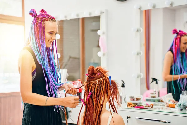 Γυναίκα κομμωτήριο υφαίνει στο κορίτσι dreadlocks τζίντζερ. — Φωτογραφία Αρχείου