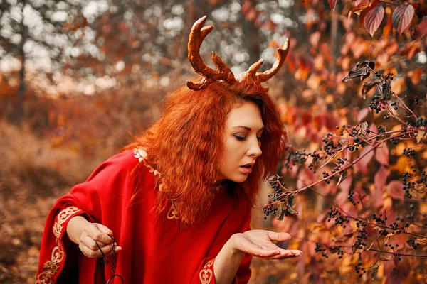 Donna in abito rosso lungo con corna di cervo nella foresta autunnale. — Foto Stock