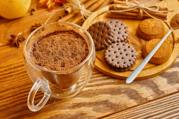 Cocoa, cookies and cinnamon sticks on wooden table.