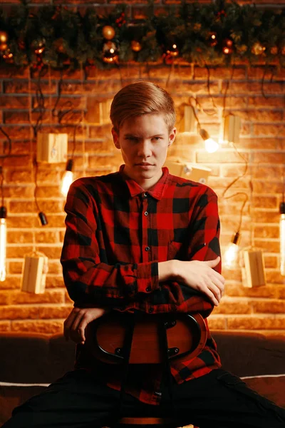 Young guy with serious face on high chair in Christmas decorations. — Stock Photo, Image