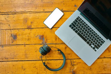 Dizüstü bilgisayar, kablosuz kulaklık ve cep telefonu ahşap masada..