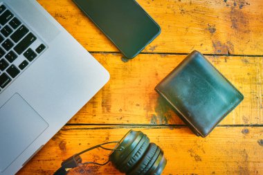 Laptop, kablosuz kulaklık, cep telefonu ve cüzdan ahşap masada..