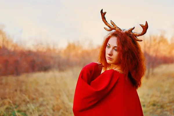 Femme en robe longue rouge avec cornes de cerf dans la forêt d'automne. — Photo
