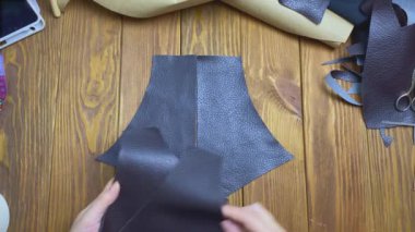 Kadın ellerinin üst görüntüsü ahşap masaya eko-deri parçaları serer..