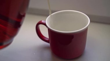 Adam cam çaydanlıktan kırmızı seramik bardağa çay döker..