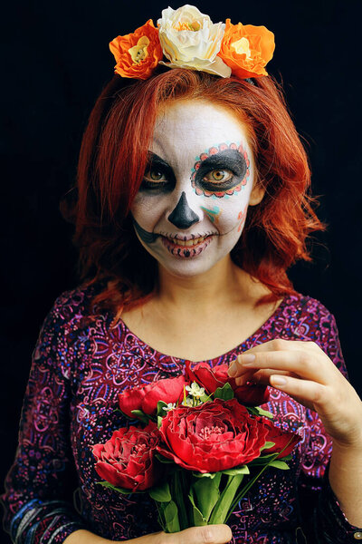 A young woman in day of the dead mask skull face art. Woman with sugar skull makeup and red hair isolated on black background.