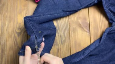 Kadınların elleri kotun üzerindeki makasla dikişleri söker..