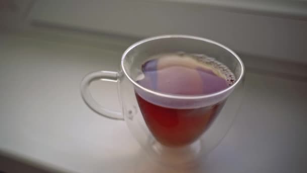 In mug with fragrant tea standing on windowsill, pour few spoons of sugar. — Stock Video