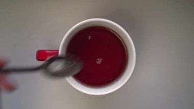 Bir fincan çaya bir kaşık dolusu şeker döken erkeklerin üst görüntüsü.