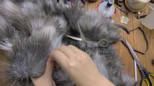Top view of seamstress hands who sew patterned clasp on grey fluffy fur. — Stock Video