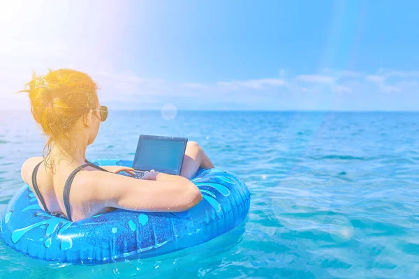 Dziewczyna spoczywa na morzu na nadmuchiwanym pierścieniu z mini-komputerem. — Zdjęcie stockowe