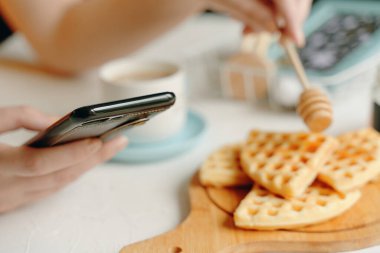 Kadın waffle, kahve ve telefonda sohbet ile kahvaltı yapıyor..