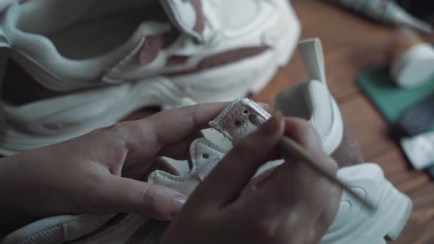 Persons hand with brush paints white sneaker. — Stock Video