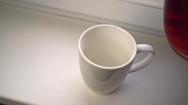 人はガラスのティーポットから香り高いお茶を白いセラミックマグカップに注ぐ. — ストック動画