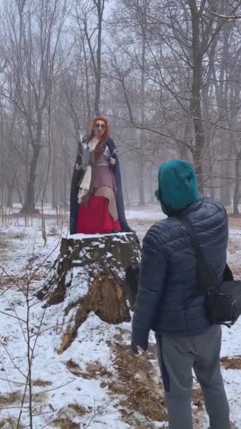 Мужчина в куртке в капюшоне стреляет в девушку-косметолога с жутким макияжем в снежном лесу. — стоковое видео