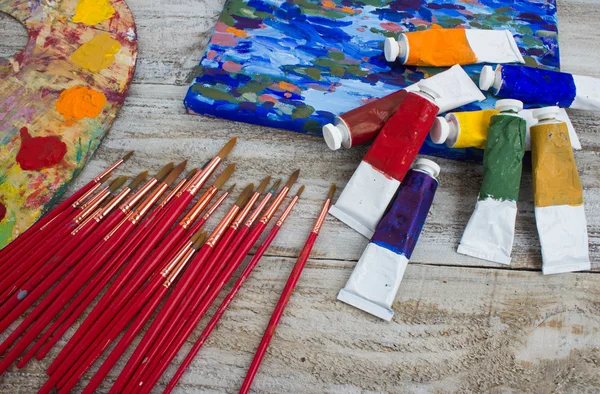 Pinceles, pintura, paleta, lienzo pintado sobre fondo de madera — Foto de Stock