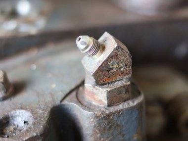Close-up of a heavily worn and rusted metallic hydraulic fitting or elbow with a threaded connection, attached to a dark industrial machine component