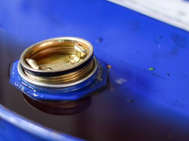 Close-up of the open bung hole and brass plug of a blue industrial drum filled with dark liquid, likely oil or lubricant.