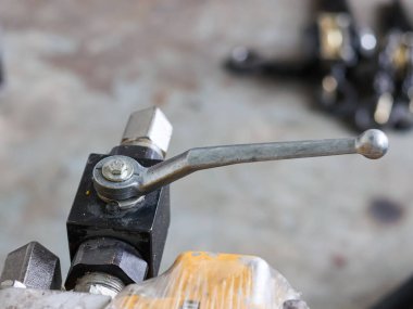 Close-up of a manual control lever on a black hydraulic valve block, connected to a yellow machine part partially wrapped in protective plastic film.