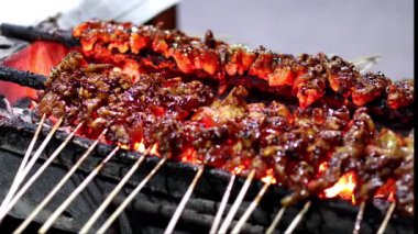 Chicken Satay or Sate Ayam skewers coated in thick peanut sauce, being grilled over glowing charcoal embers on a street vendor's portable grill at night.
