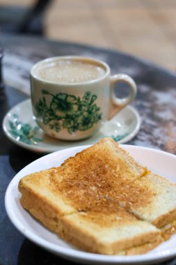 Geleneksel bir porselen fincanda sıcak Kopi Susu 'nun klasik bir kahvaltısı (yoğunlaştırılmış sütle kahve) ve arka planda hafif bulanık Kaya tostu dilimi..
