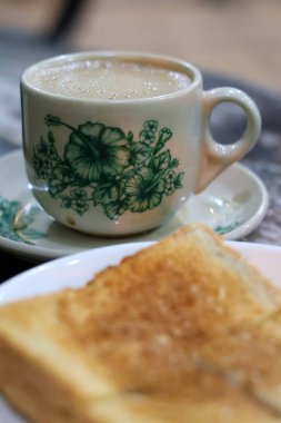 Geleneksel bir porselen fincanda sıcak Kopi Susu 'nun klasik bir kahvaltısı (yoğunlaştırılmış sütlü kahve) ve ön planda hafif bulanık Kaya tostu..