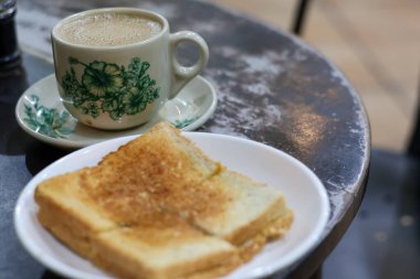 Geleneksel bir porselen fincanda sıcak Kopi Susu 'nun klasik bir kahvaltısı (yoğunlaştırılmış sütlü kahve) ve ön planda hafif bulanık Kaya tostu..