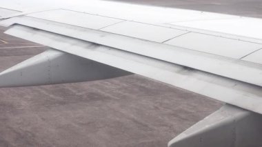 İniş veya kalkış sırasında kanatları açık olan uçak kanadı, bulutlu bir günde aşağıdaki pisti veya pisti gösteren kabin penceresinden görülüyor..