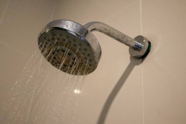 Krom bir duş başlığının yakın plan karo bir duvara bağlı, aktif olarak akan su, temiz, açık renkli yüzeye karşı güçlü akıntılar ve damlacıklar gösterir.