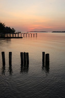 Sade, sade, ahşap iskele gün batımında suyun üzerinde uzanan, sakin su ve kumsalın üstündeki yumuşak alacakaranlık renkleriyle.