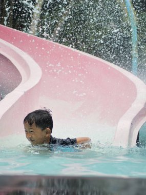Genç bir çocuk yüzükoyun yeşil bir su kaydırağında yüzükoyun yüzükoyun yüzükoyun kayıyor. Yüzüne su sıçrıyor. Açık su parkında heyecanlı bir yolculuğun tadını çıkarıyor..