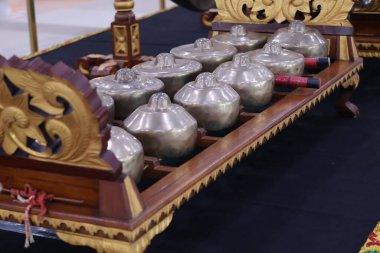 Bir Bonang Barung ya da Panerus 'a yakın bir perspektif, yontulmuş ahşap bir çerçeve üzerinde bir sıra küçük, son derece parlak bronz gonglara sahip bir Cava ya da Bali gamelan enstrümanı..