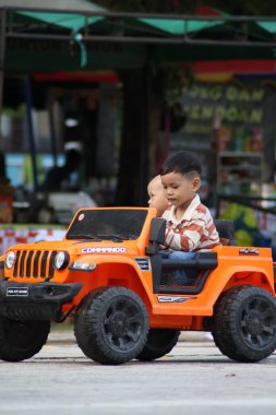 Balikpapan-Endonezya 25 Ekim 2025 tatlı bir Asyalı çocuk bir yolcuyla birlikte turuncu elektrikli bir Jeep 