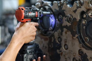 Balikpapan-Endonezya 28 Ekim 2025 Sanayi bakımı sırasında büyük, kirli, ağır bir motor veya makine muhafaza cıvatasını sıkmak veya çıkarmak için pil gücüyle çalışan bir İngiliz anahtarı kullanıyor.