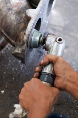 Ağır metal endüstriyel pompa ya da turbo şarj kutusu kabarık yüzeyi pürüzsüz ve cilalamak için aşındırıcı tekerleği olan bir pnömatik zar öğütücü kullanan bir işçi..