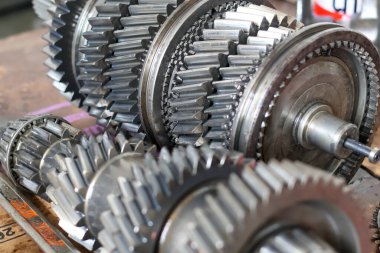 Parçalanmış iletim bileşenlerinin yakın çekimleri, bir atölyede incelemeye, onarmaya ya da yeniden monte etmeye hazır parlak metal dişli ve şaftları gösteriyor.