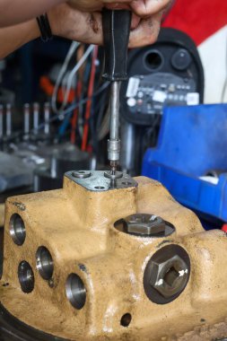 Makine bakımı ya da onarım sırasında ağır hidrolik ya da endüstriyel valf gövdesinden küçük bir vidayı çıkarmak için tornavida kullanan bir işçiye yakın çekim.