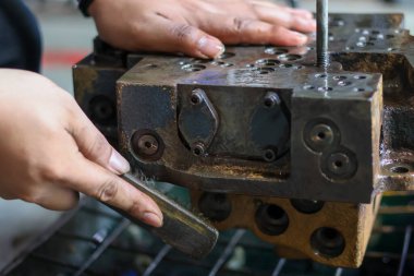 Ekipman bakımı sırasında metal tel fırça kullanarak ağır bir hidrolik kapakçık yüzeyinden aşınma ve kir temizleyen bir işçiye yakın plan..