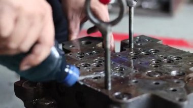 İşçi, büyük, ağır bir hidrolik kapakçığı şişeden çıkan sıvıyla duruluyor. Endüstriyel ekipman tamir atölyesinde temizlik işlemi sırasında kritik bir adım..