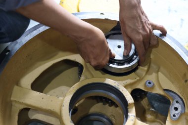 Tamircinin elleri, bir montaj ya da onarım işlemi sırasında büyük, hassas bir topu, ağır bir endüstriyel makine bileşeninin sarı kaplamasına ya da merkezine yerleştiriyor..