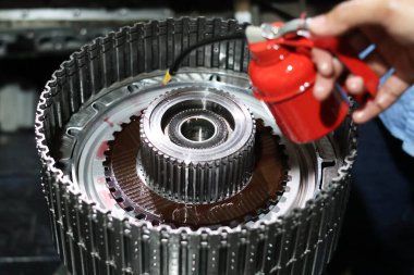 Teknisyen, otomatik şanzıman montajı sırasında debriyaj çantasına ve metal dişli bileşenlerine küçük kırmızı bir pompa dağıtıcısından yağ uyguluyor..