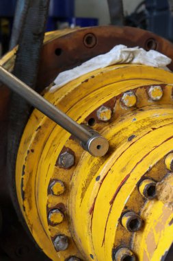 Bir teknisyenin eli, büyük bir T-kulpu kullanıyor. Tamir ve bakım sırasında endüstriyel bir son sürüş ünitesinin ağır vidalanmış, yıpranmış sarı konutu..