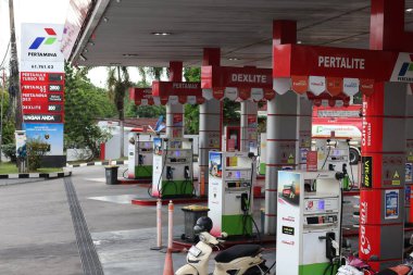Balikpapan-Endonezya 11 Kasım 2025 Yakıt dağıtıcıları ve pompaları, Pertamina marka ürünler Pertalite ve Dexlite, Endonezya 'nın hareketli bir benzin istasyonunda motosikletle.