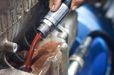 Bir tamirci metalik bir motora ya da dişli kutusuna doldurma başlığı kullanarak parlak kırmızı şanzıman sıvısı döküyor.